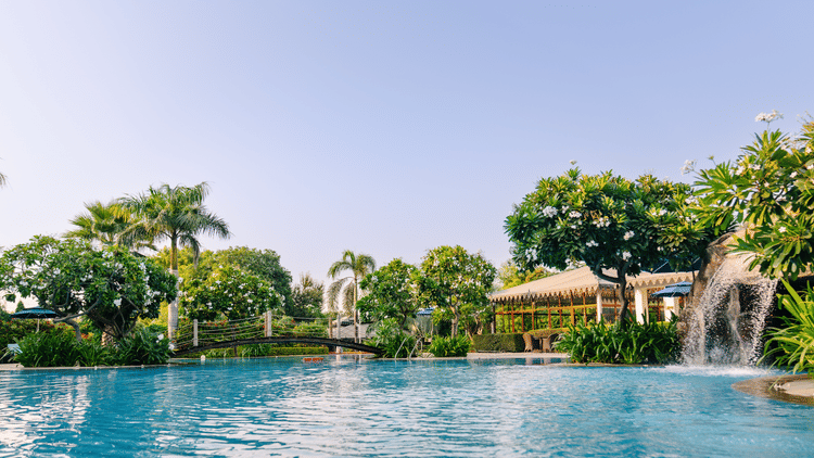 Swimming pool with a small waterfall on the side and a bridge in the centre